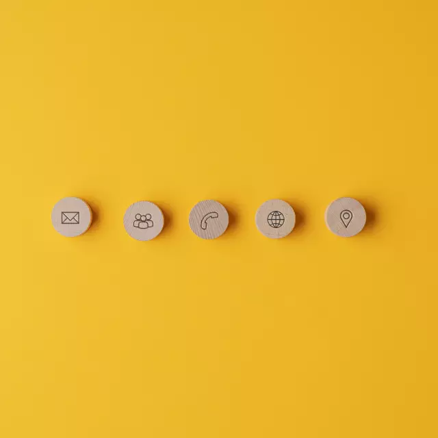 Five wooden cut circles with contact and information icons on them placed in a row over yellow background.